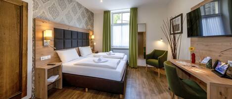 A modern hotel room with a large bed, a desk, a chair, and a TV.