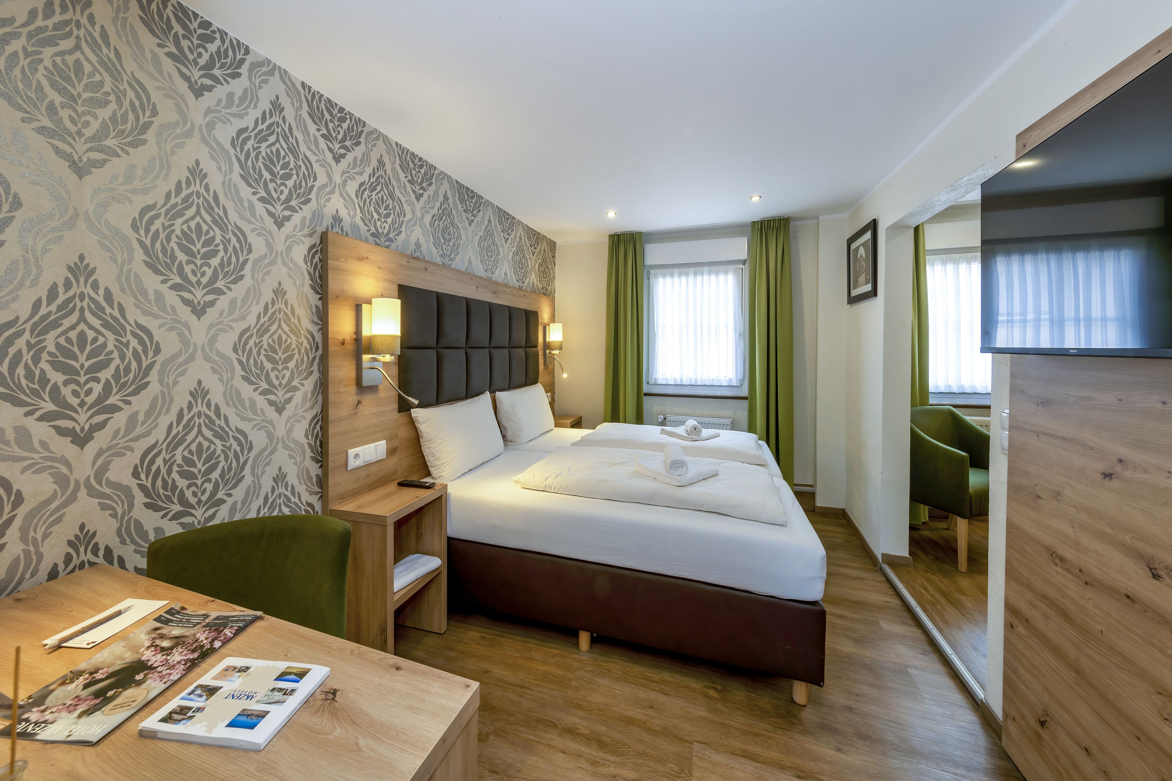 A hotel room with a large bed, a wooden headboard, a desk with a chair, and a TV.