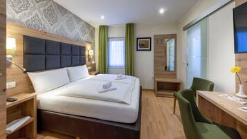 A modern hotel room with a large bed, a desk, a chair, a mirror, and a window with curtains.
