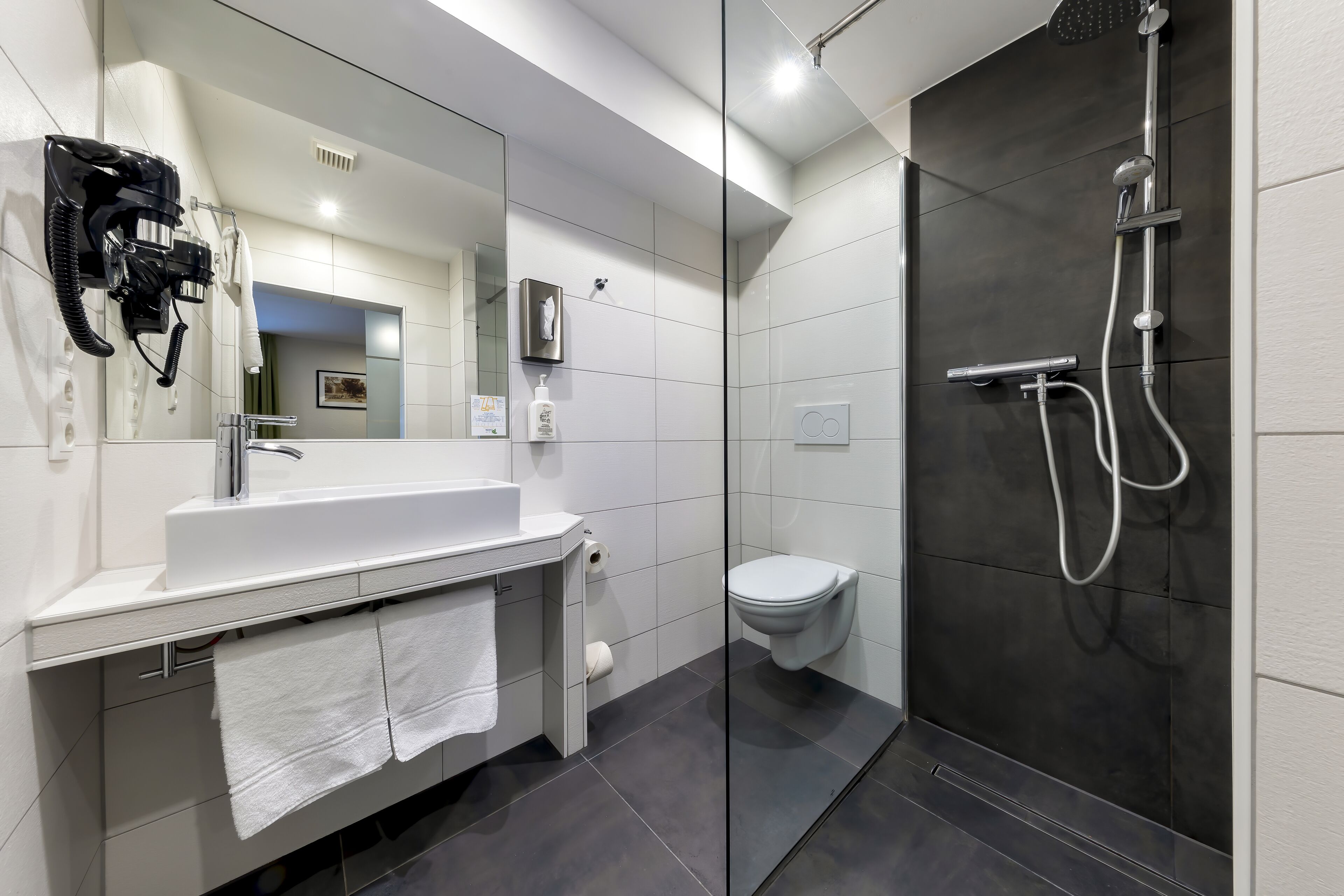 A modern bathroom with a white sink, mirror, and a glass-enclosed shower area.