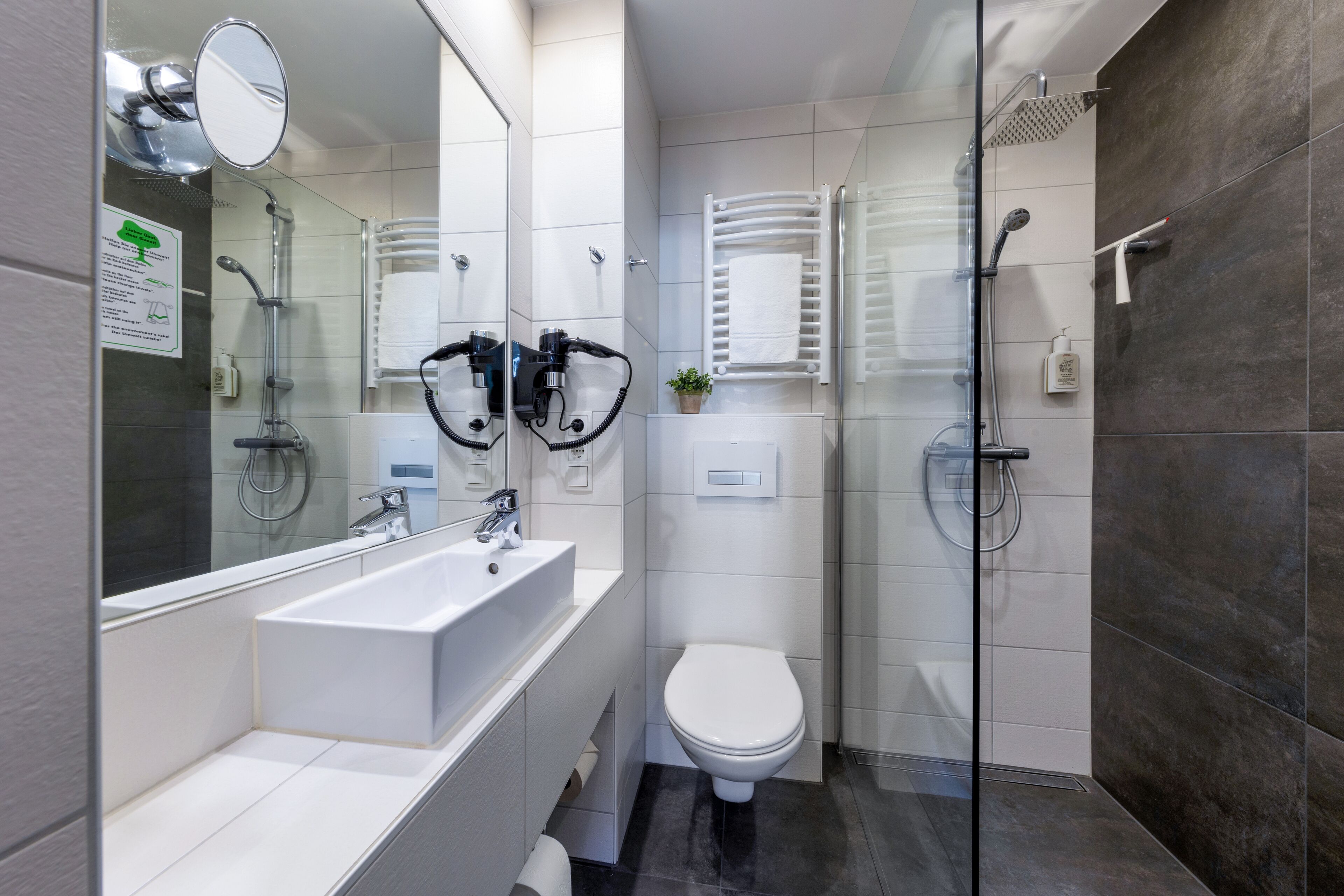 Une salle de bain moderne avec un grand miroir, un lavabo blanc, des toilettes et une douche séparée par des parois en verre.