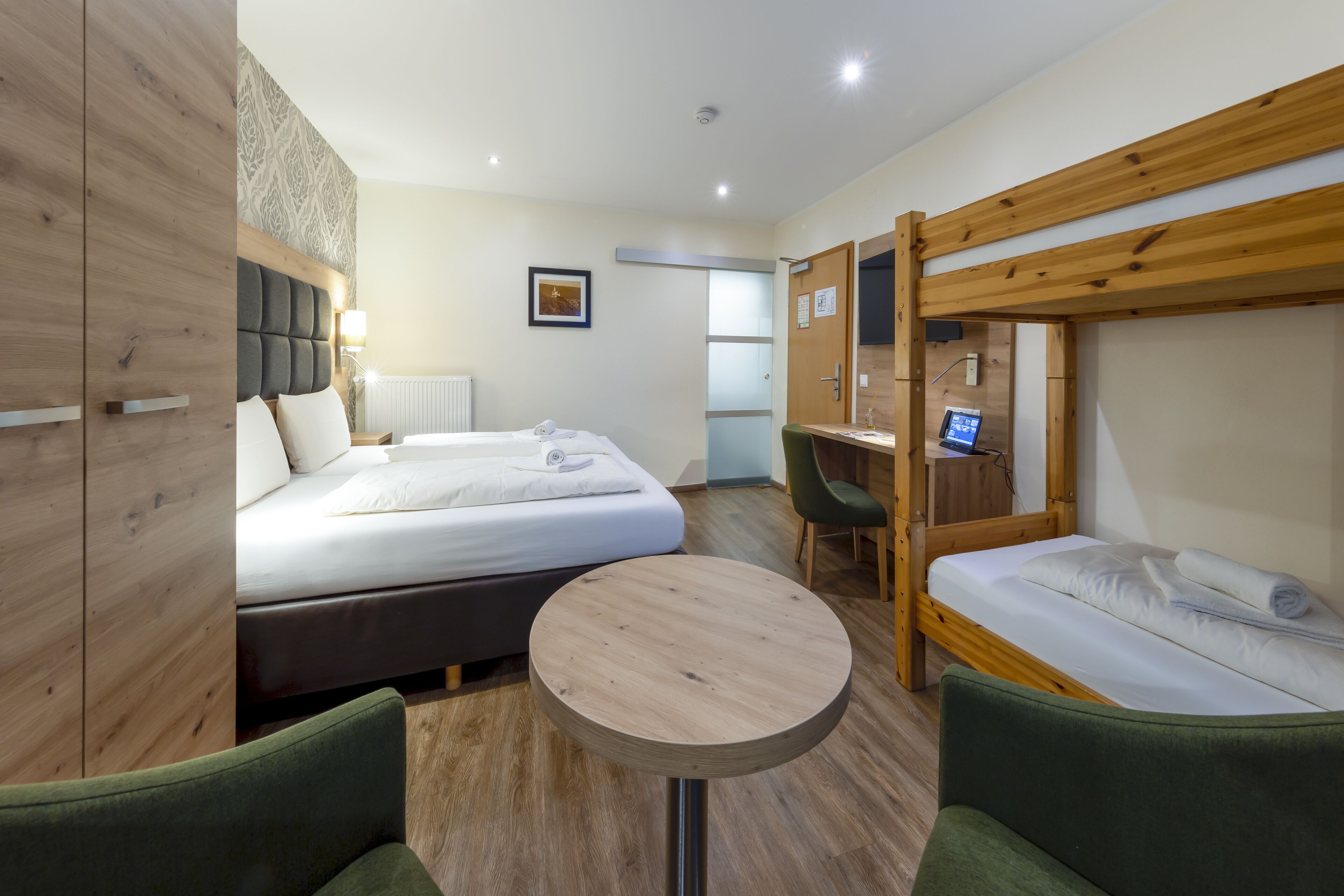 A hotel room with a bed, a desk, a chair, and a small table.