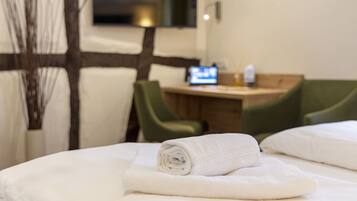 A neatly made bed with white linens, a small desk with a computer, and green chairs in a hotel room.