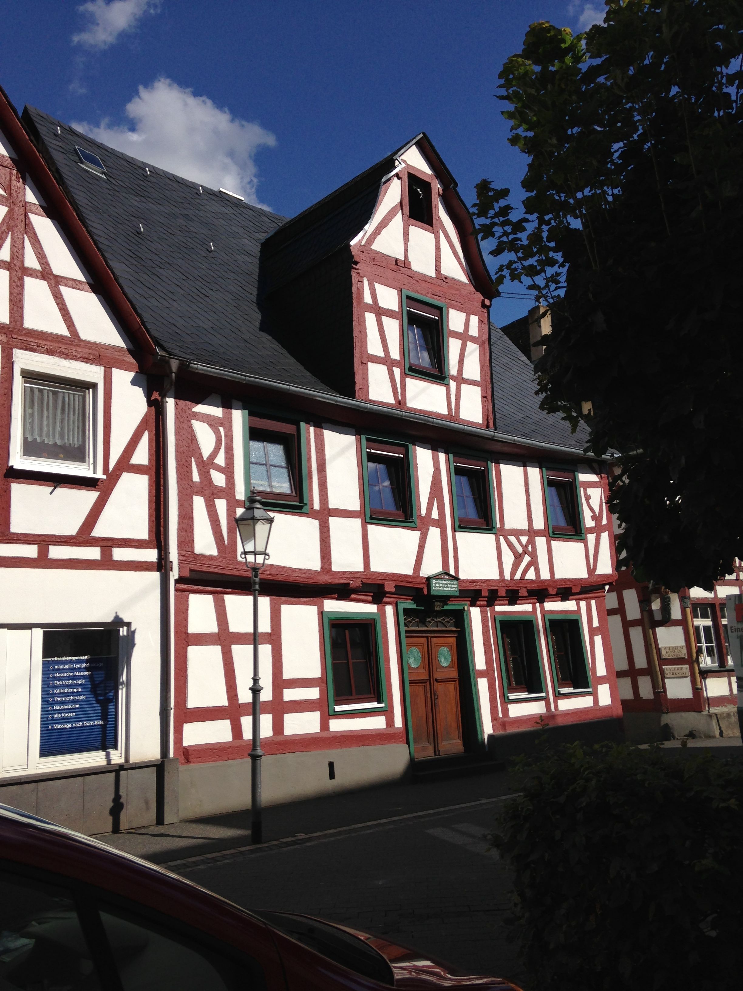 A traditional half-timbered building with a steep gable roof, a central entrance with a wooden door, and a small window with a green frame.
