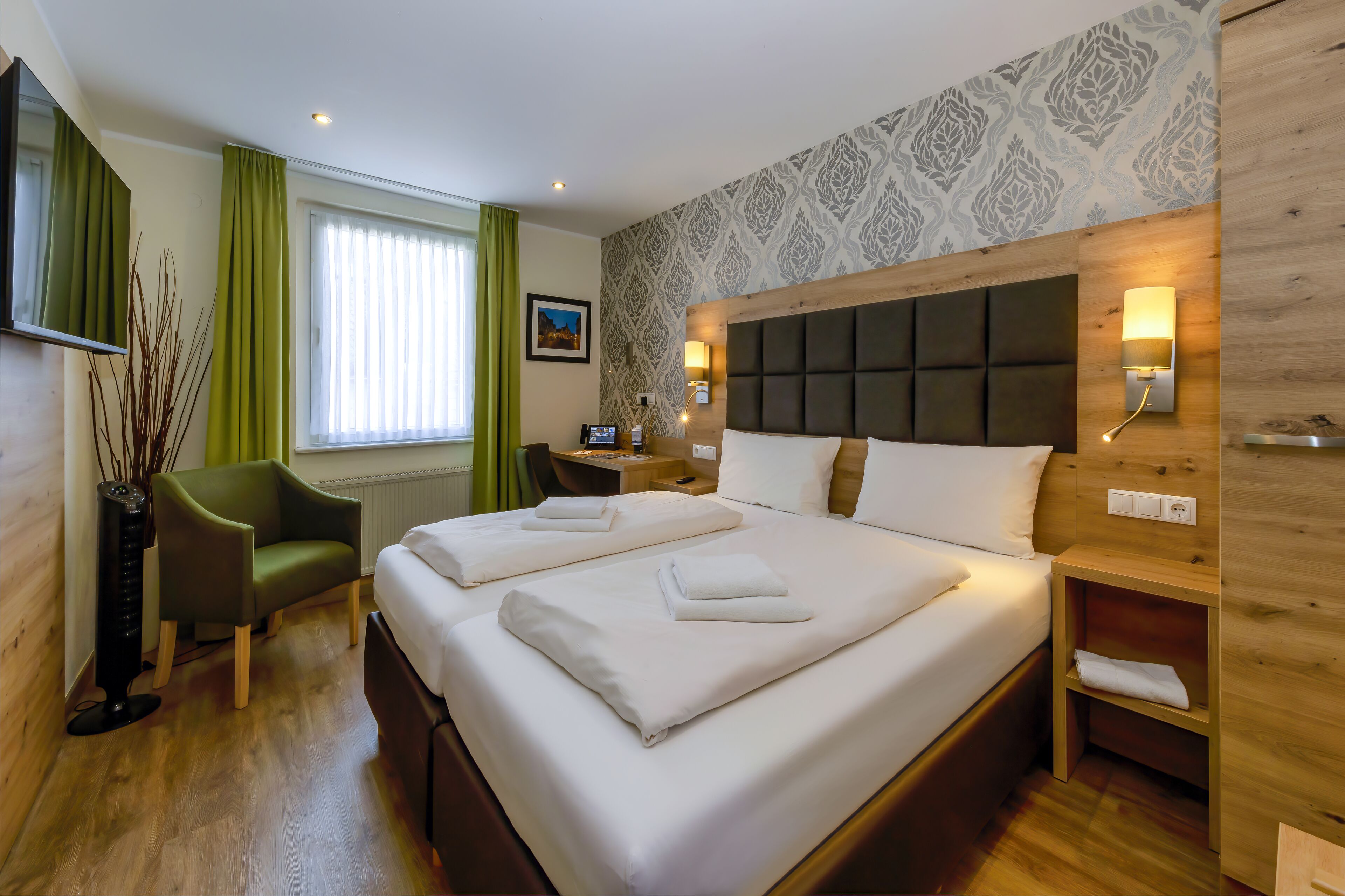 Une chambre d’hôtel avec un grand lit, deux tables de chevet, un bureau, une chaise et une fenêtre avec des rideaux.