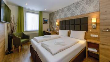 Habitación de hotel con una cama grande, dos mesitas de noche, un escritorio, una silla y un ventanal con cortinas.