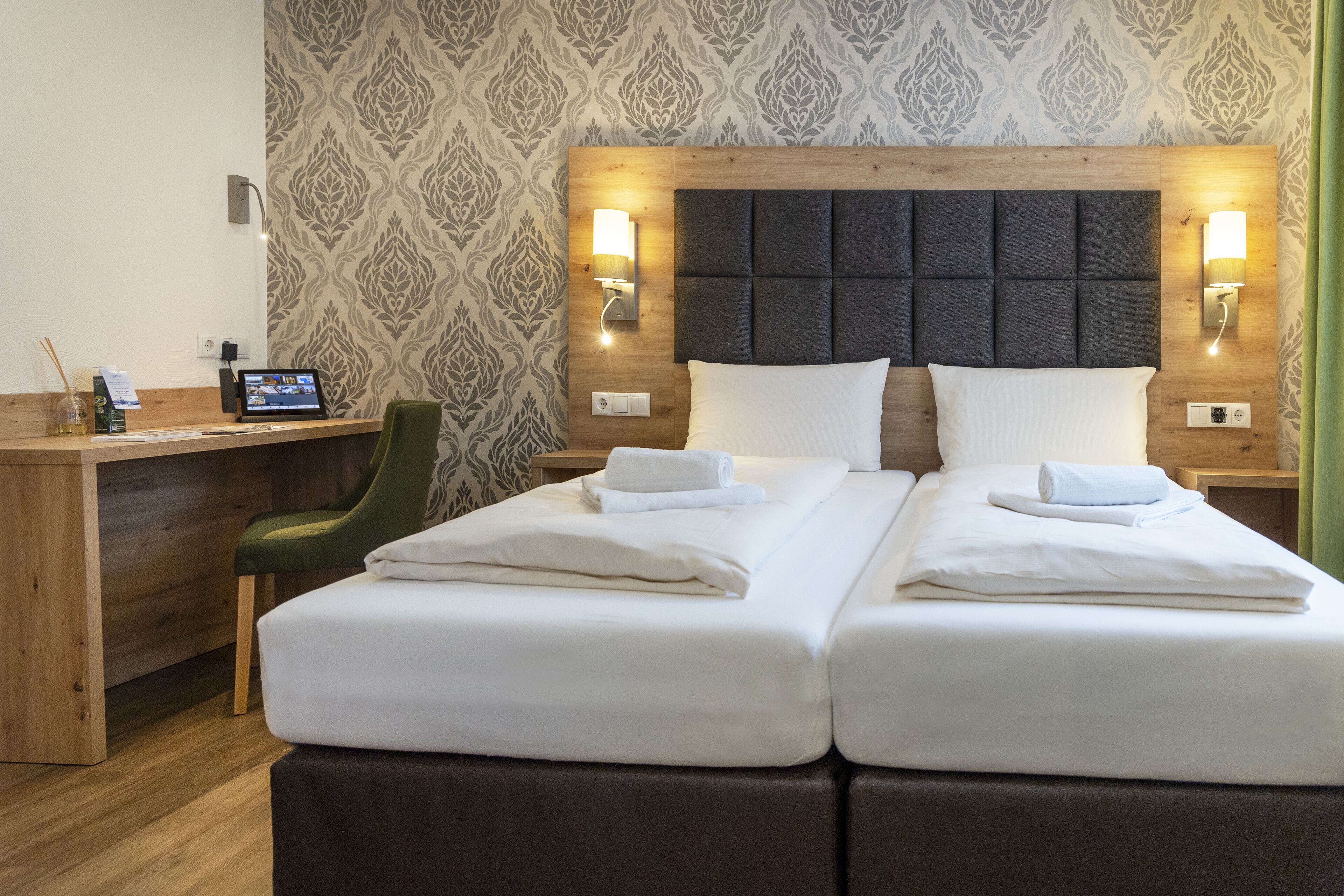 A hotel room with a double bed, a desk, a chair, and a laptop.