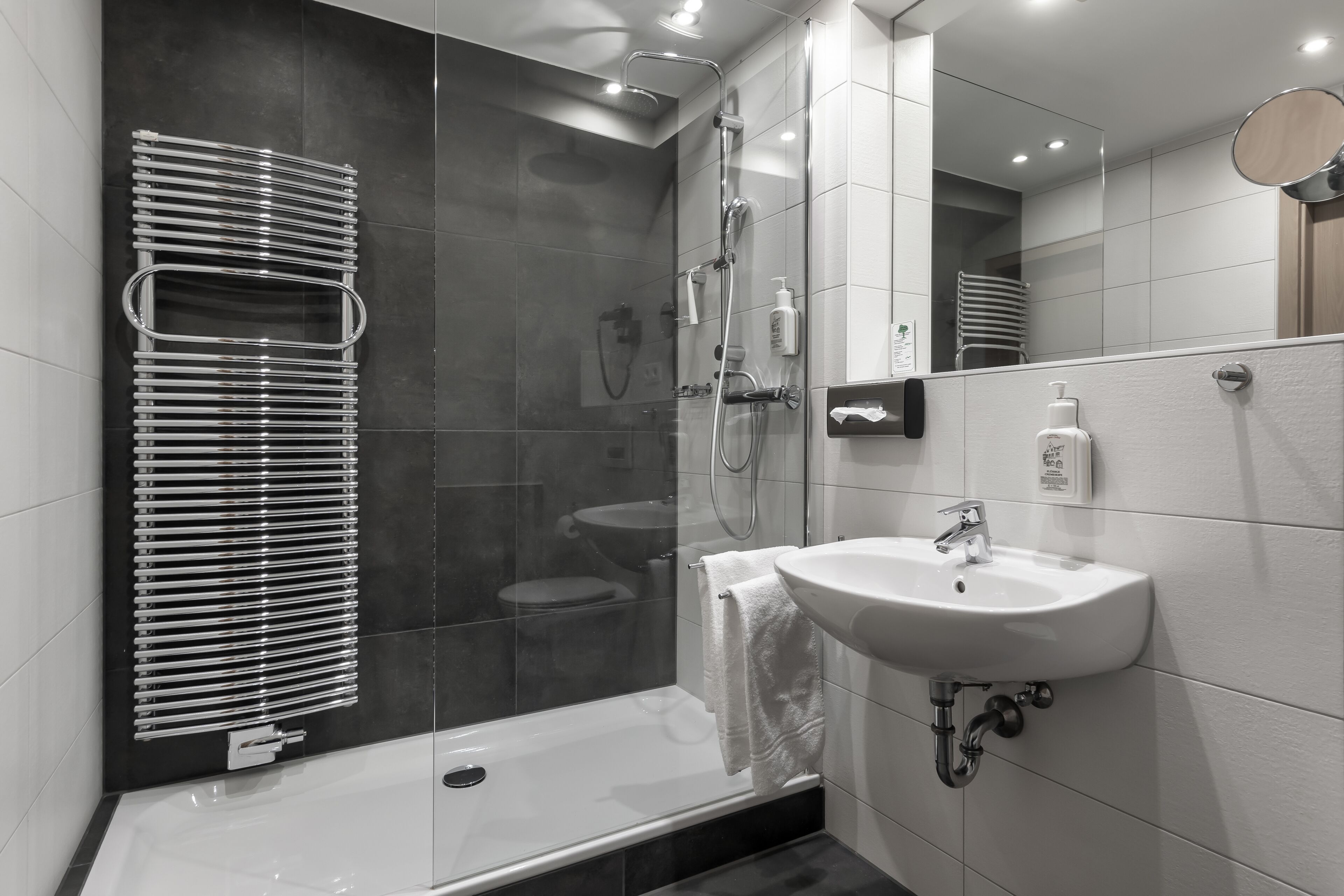 A modern bathroom with a glass-enclosed shower, a white sink, and a towel rack.