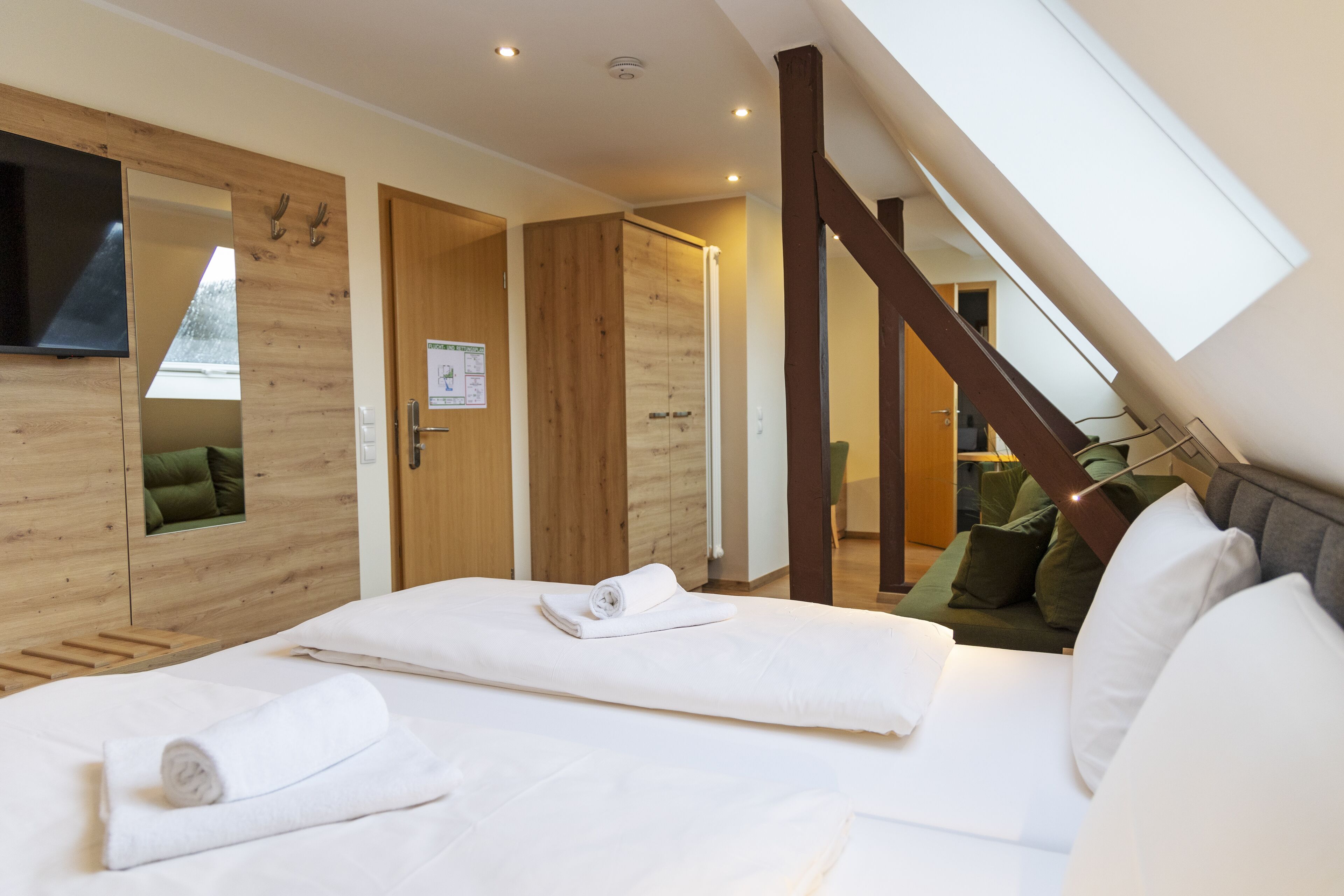 Une chambre d’hôtel avec un lit, une armoire en bois, un miroir et une lucarne.