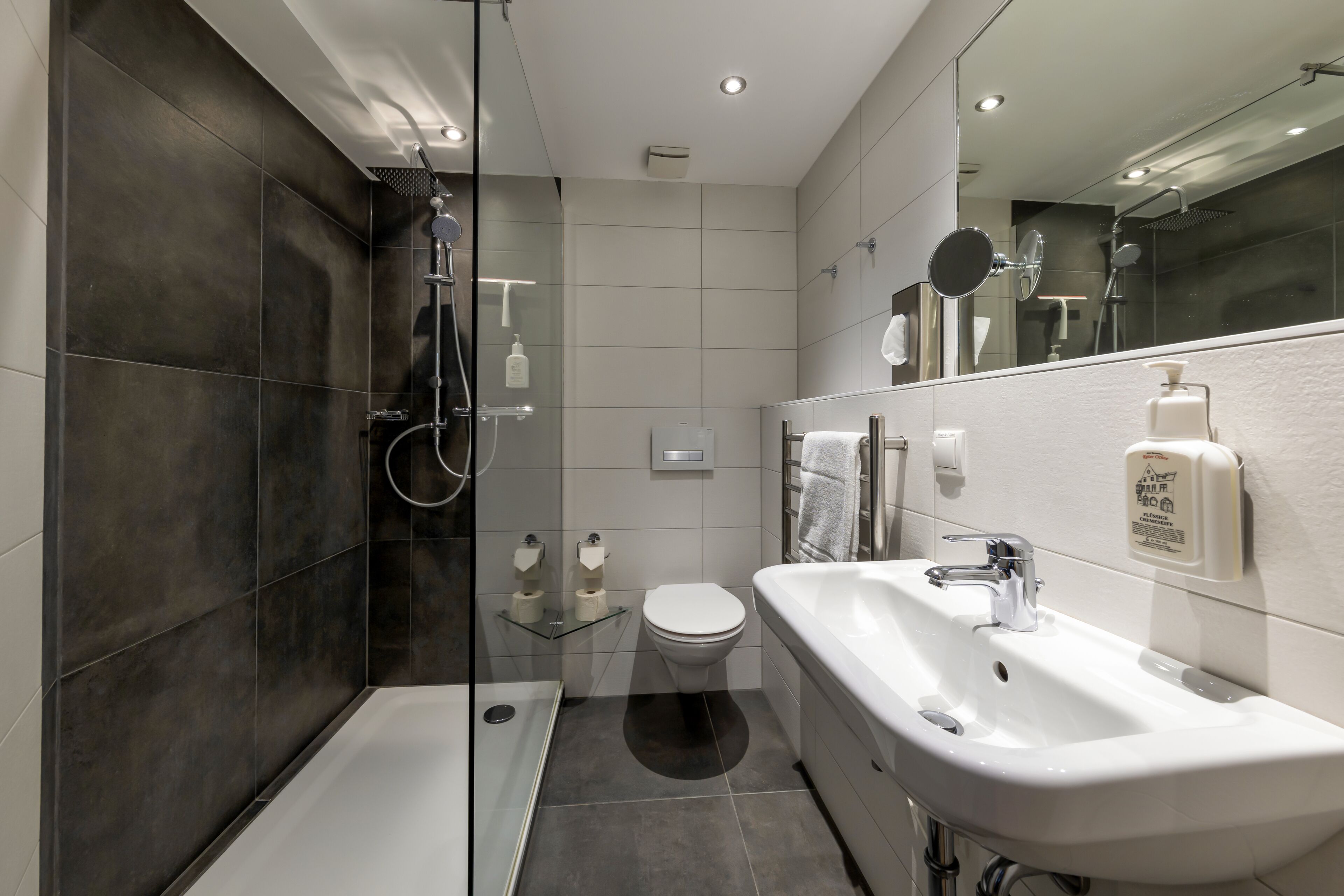 A modern bathroom with a glass-enclosed shower, a white sink, and a toilet.