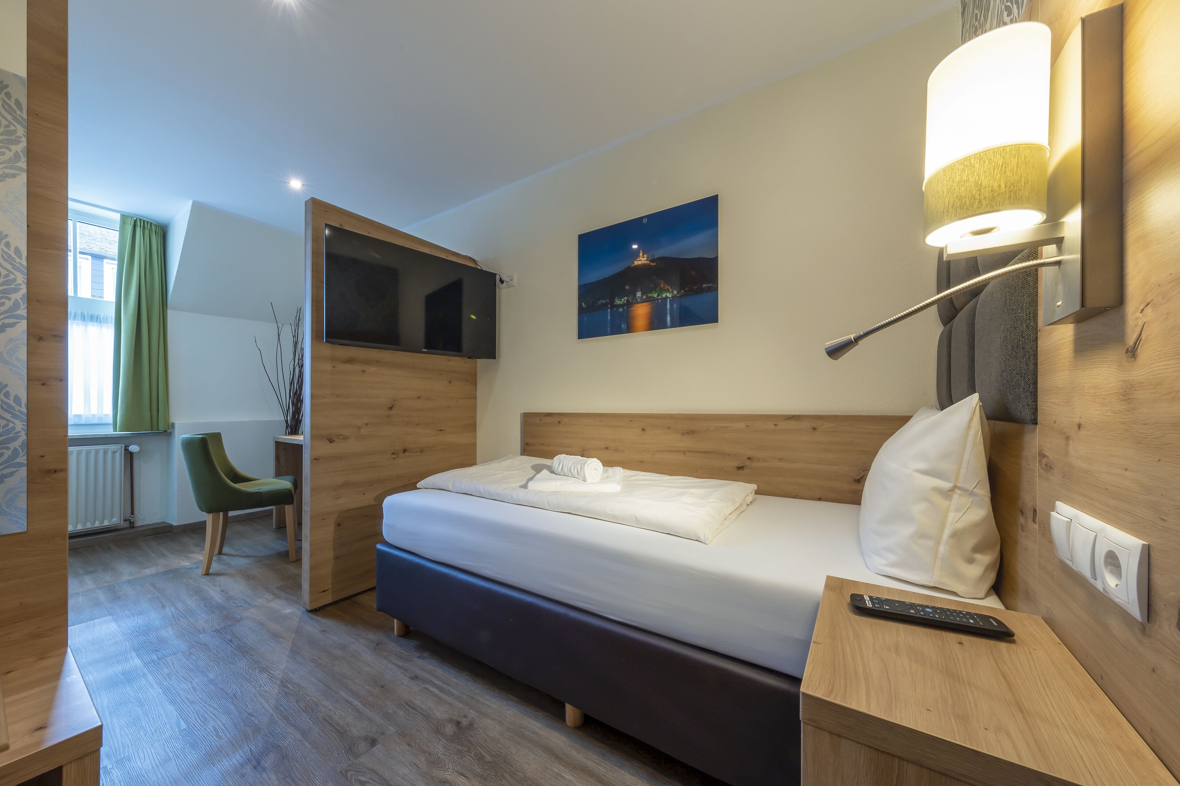 Una habitación de hotel moderna con una cama de madera, una mesita de noche con un control remoto, una lámpara de pared y un cuadro de un paisaje urbano.