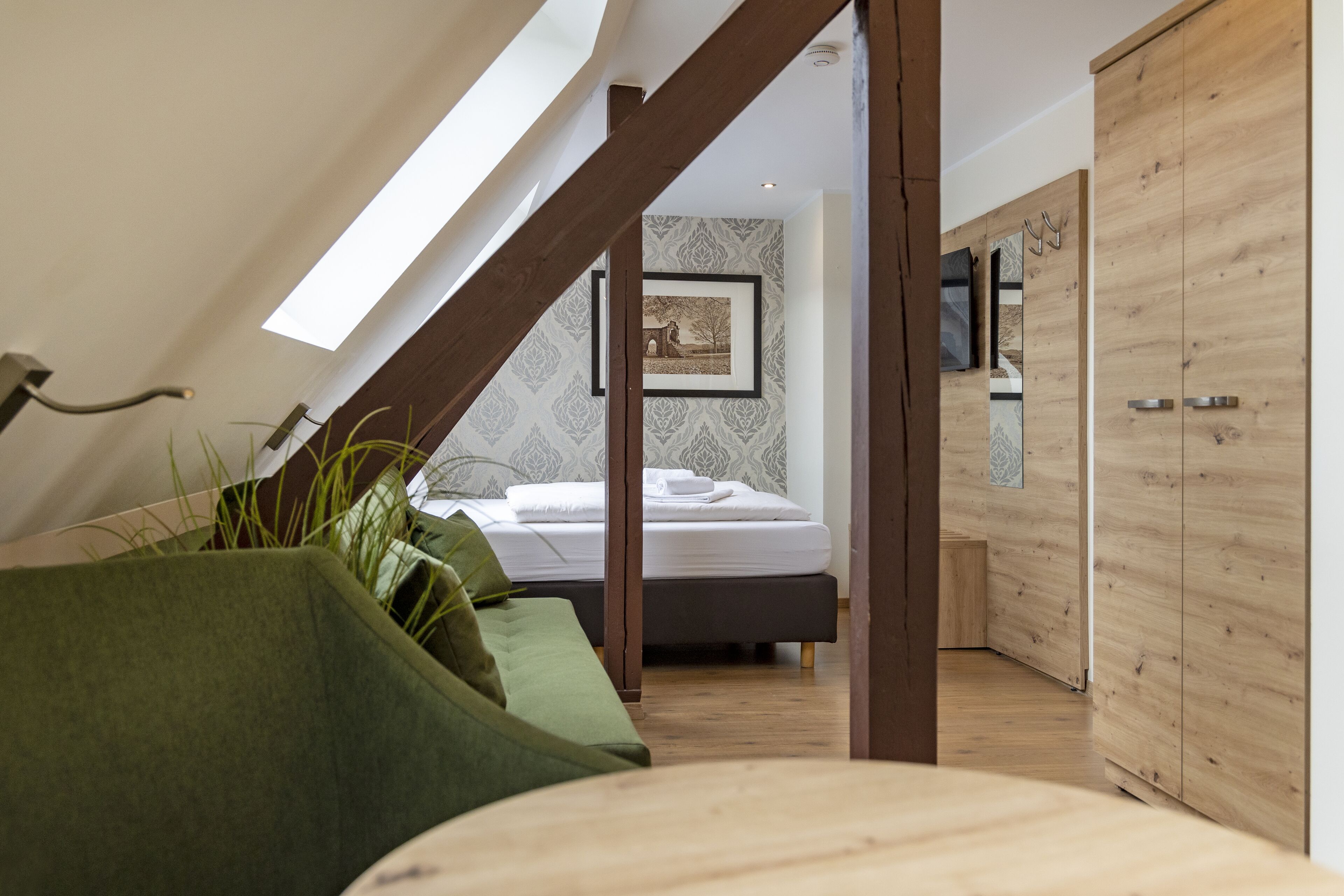 Une chambre avec un plafond en pente, un lit, une armoire en bois et un tableau encadré au mur.