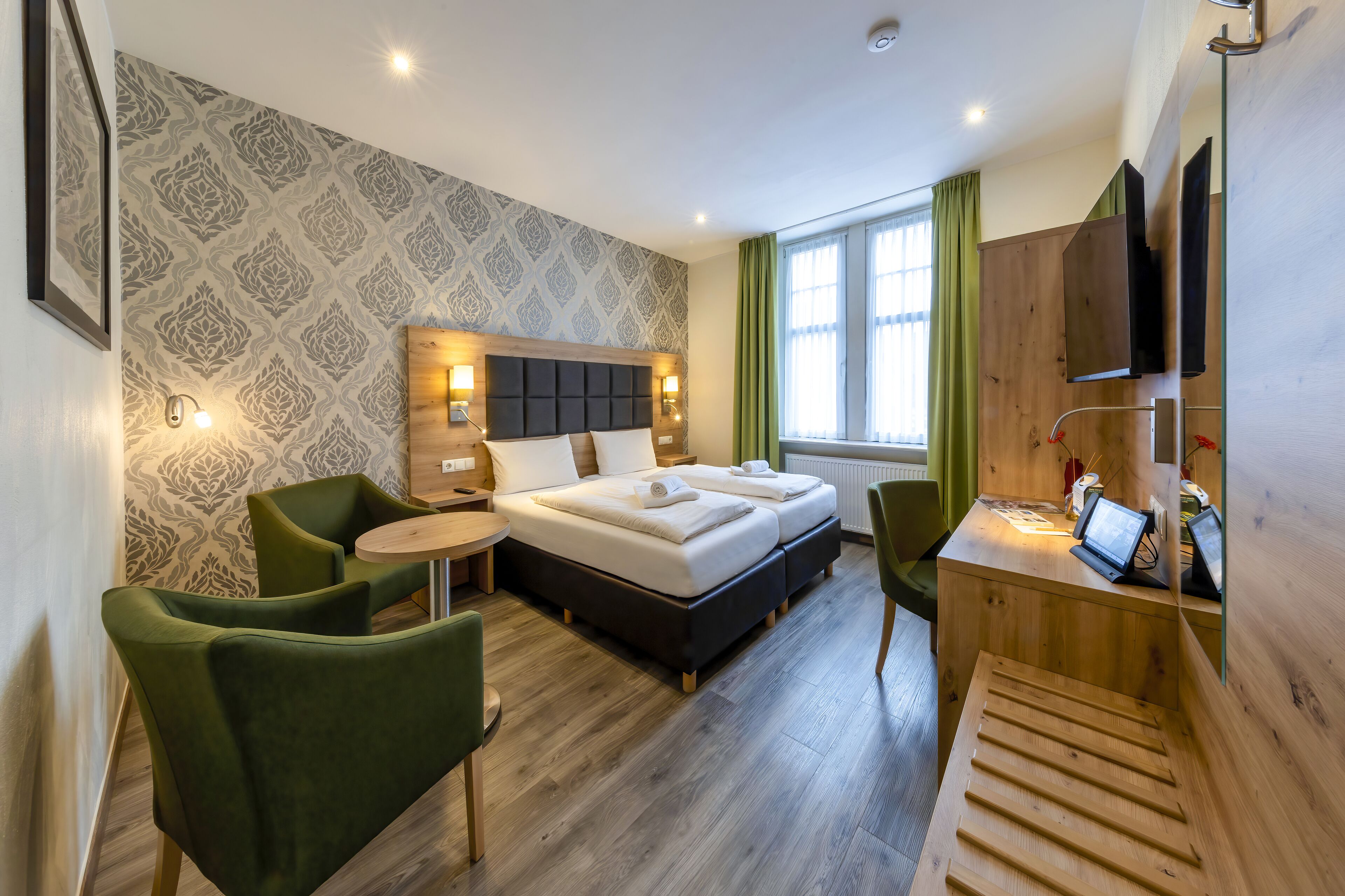 A modern hotel room with a large bed, a desk with a laptop, and a green chair.