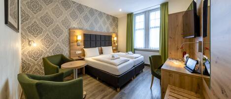 A modern hotel room with a large bed, a desk with a laptop, and a green chair.