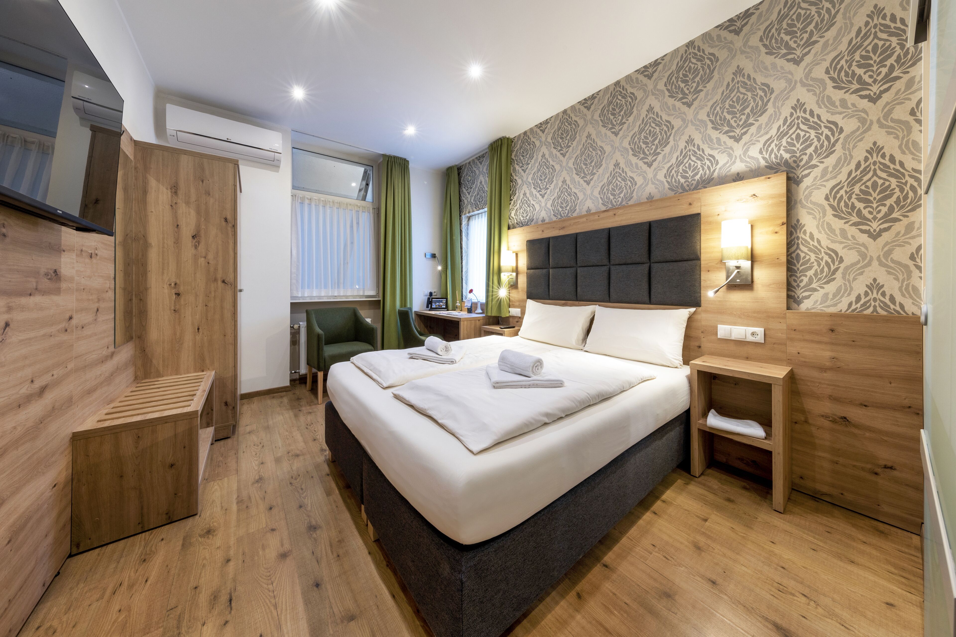 Una habitación de hotel moderna con una cama grande, cabecera de madera, mesitas de noche y un escritorio con silla.
