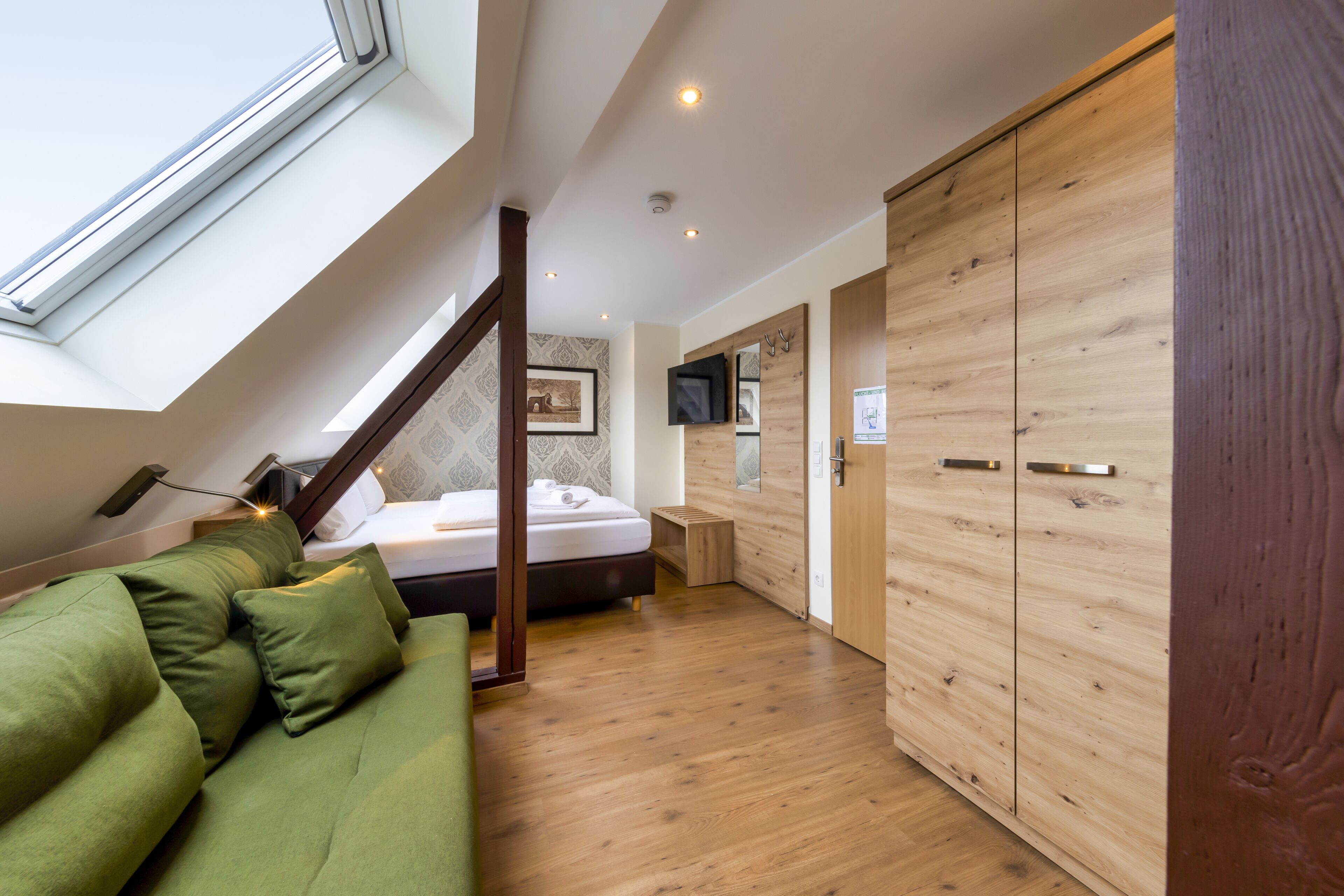 A modern bedroom with a skylight, wooden wardrobe, and a green sofa.