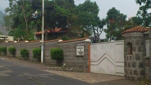 A gated property with a stone wall, a metal gate, and a small building with a tiled roof. - Hotel Vista Dorada Hacia Dios (Santiago Atitlán)