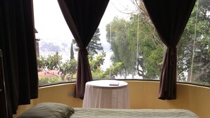 A single bed with a quilted mattress, a small round table with a white tablecloth, and a window with curtains.