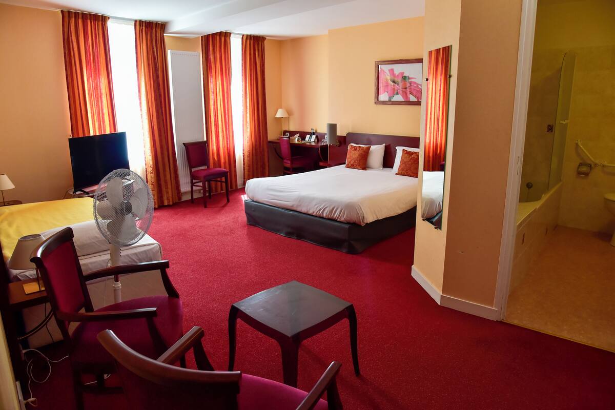 Ein Hotelzimmer mit einem Bett, einem Schreibtisch mit Stuhl, einem Fernseher, einem Ventilator und einem Badezimmer.