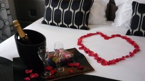A bed with black and white patterned pillows, a tray with a bottle of champagne, glasses, and a heart-shaped decoration made of rose petals. - Logis Hôtel Le Pélican & son restaurant (Vernantes)