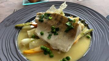 A plate of food with a fish fillet, peas, and vegetables in a creamy sauce.