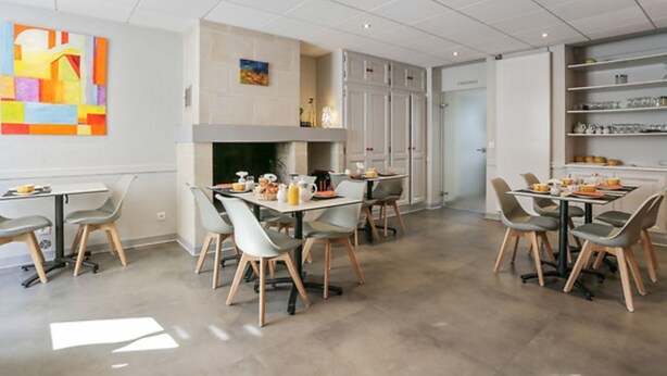 A modern dining area with two tables, chairs, a fireplace, and artwork on the walls. - Logis Hôtel Le Pélican & son restaurant (Vernantes)