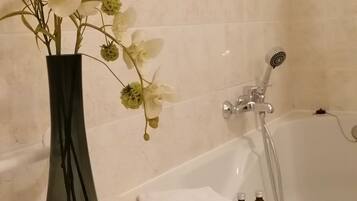 Un baño con una bañera, un florero con flores blancas y una pila de toallas blancas.