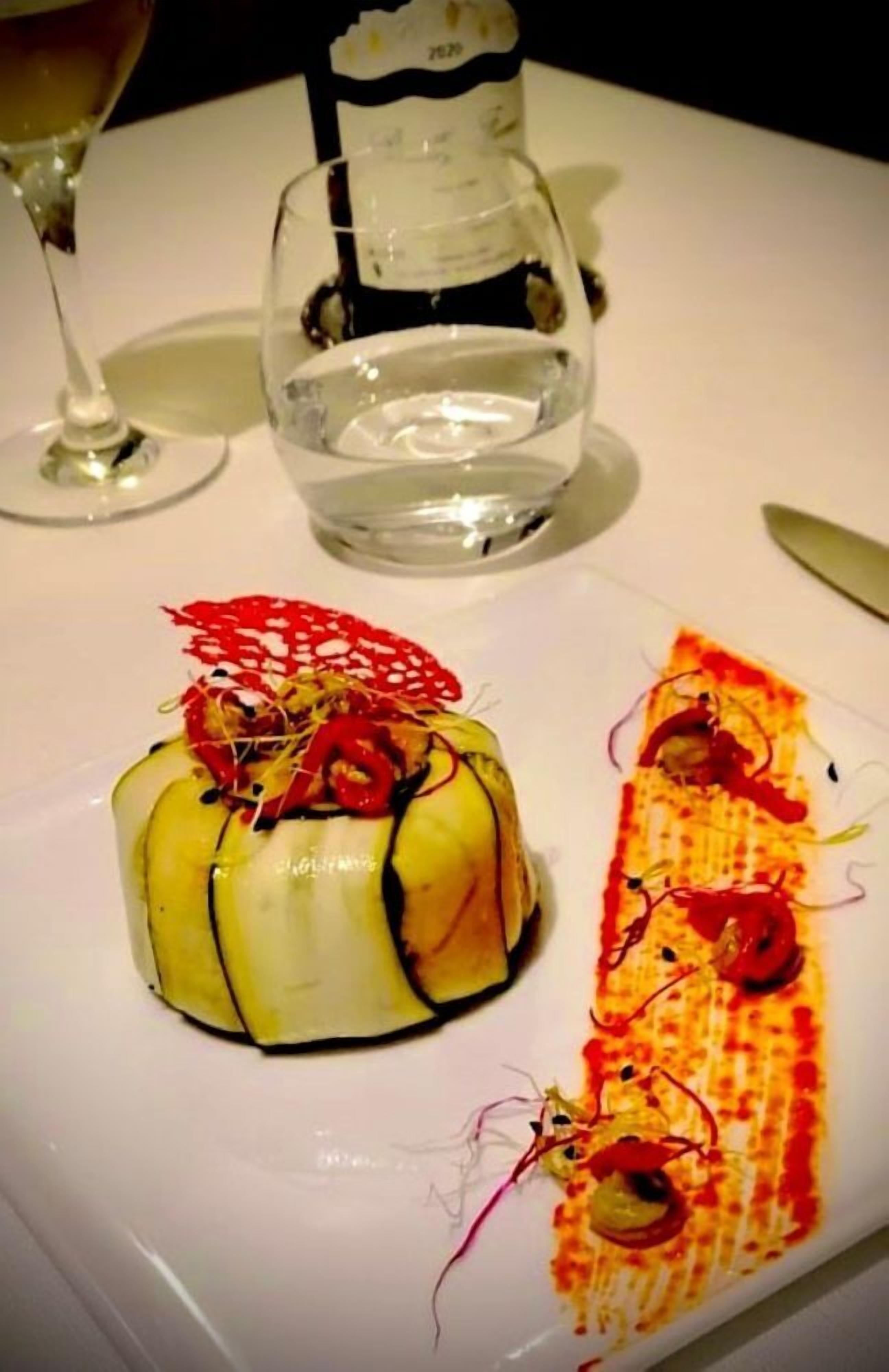Ein Dessertteller mit zwei kunstvoll gestalteten Schalen, einem Weinglas und einem Wasserglas auf weißem Tisch.