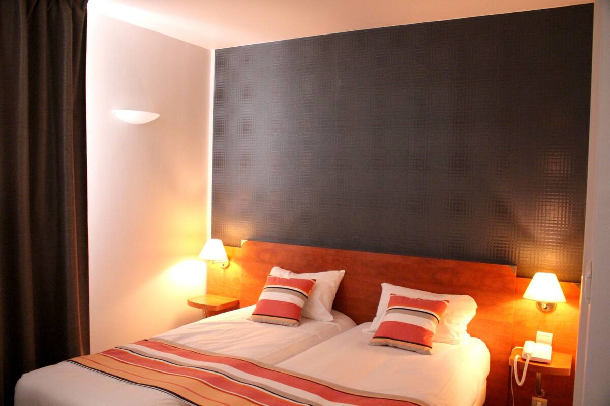 Ein Hotelzimmer mit einem Bett, zwei Nachttischlampen, einem Telefon und einem Vorhang.