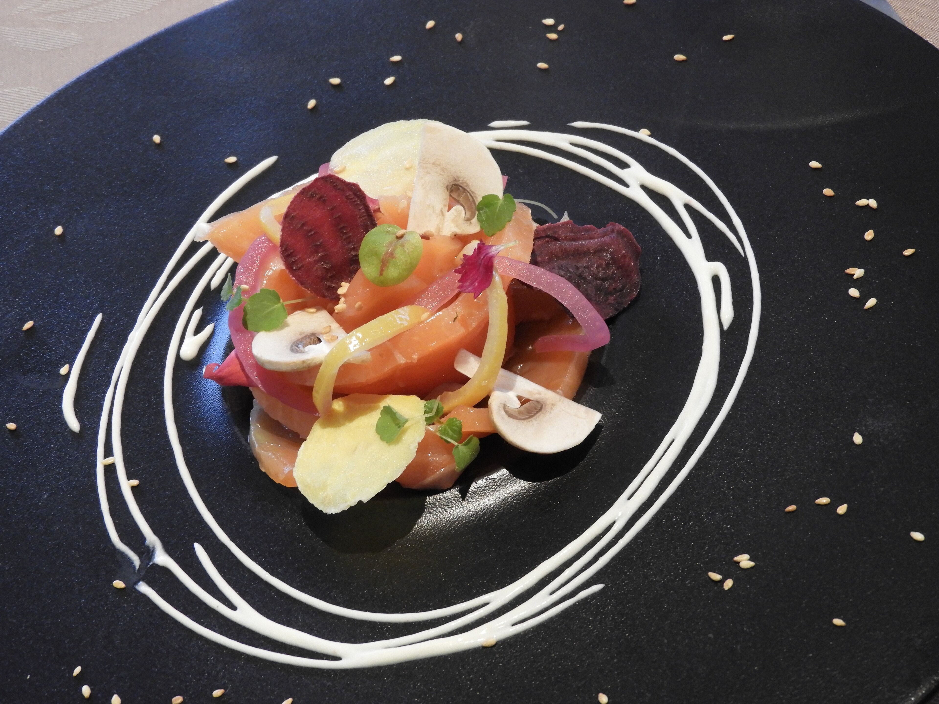 Un plato negro con un remolino de salsa blanca, coronado con diversos vegetales y guarniciones.
