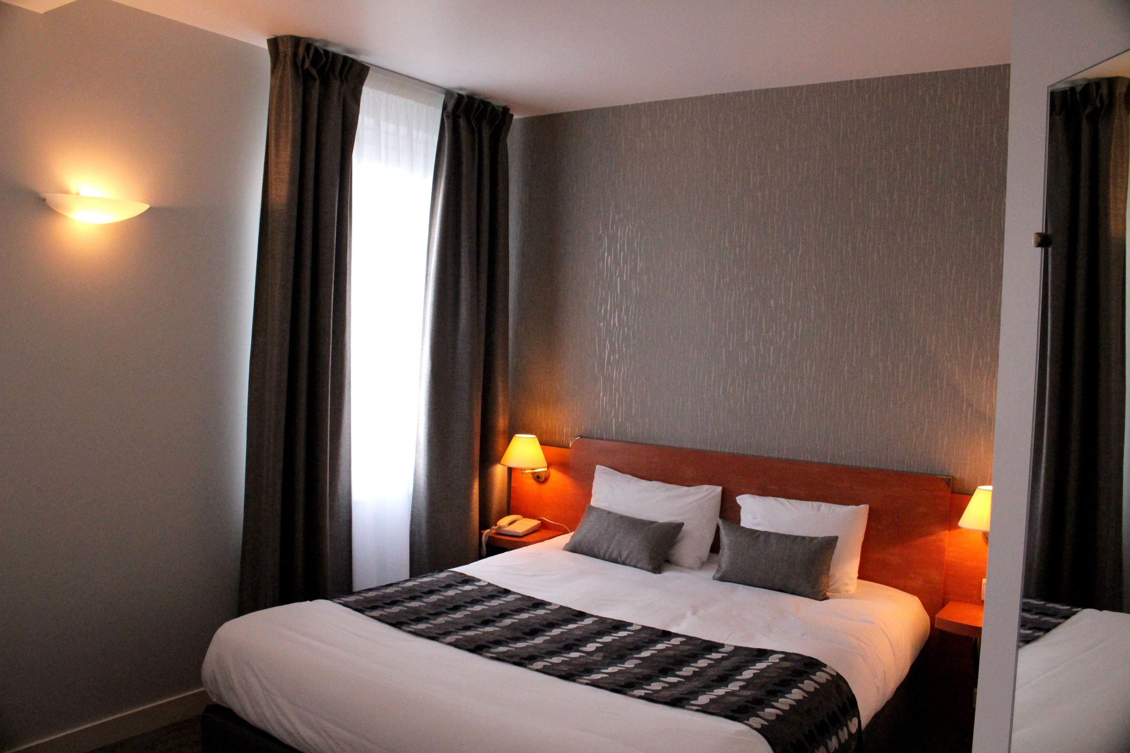 Une chambre d’hôtel avec un grand lit, deux lampes de chevet, une table de chevet et une fenêtre avec des rideaux.