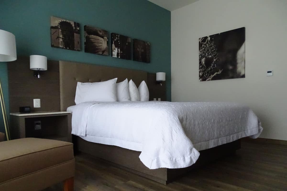 Habitación de hotel con una cama grande, una mesita de noche, una lámpara y una obra de arte colgada en la pared.