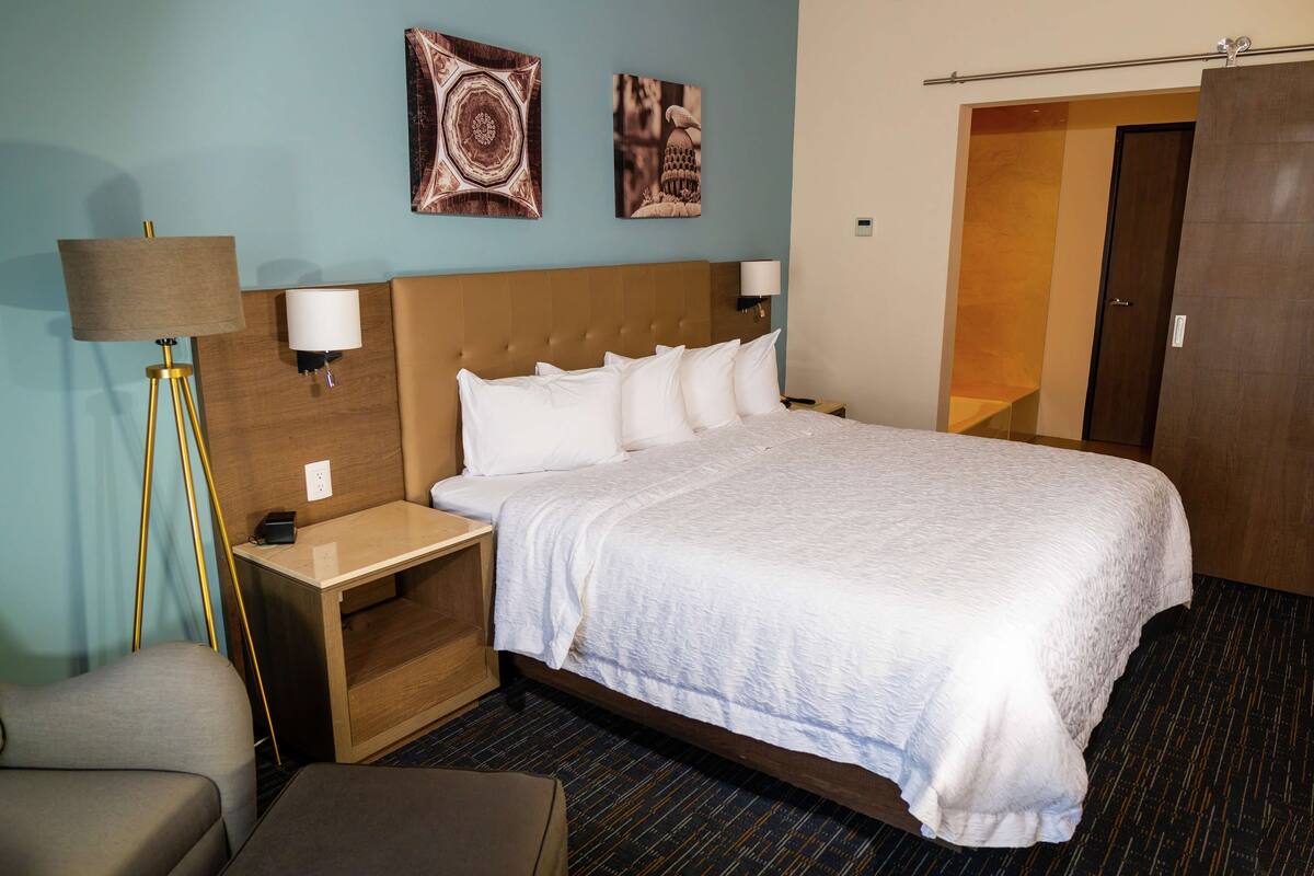 Habitación de hotel con una cama grande, una mesita de noche, una lámpara y dos lámparas de pared.