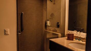 Un baño moderno con ducha de vidrio, tocador con espejo y artículos de aseo.