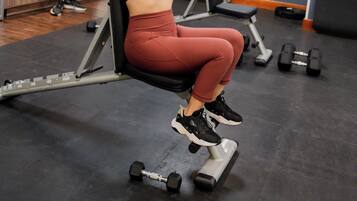 A gym with exercise equipment, a person using a machine, and another person in the background.
