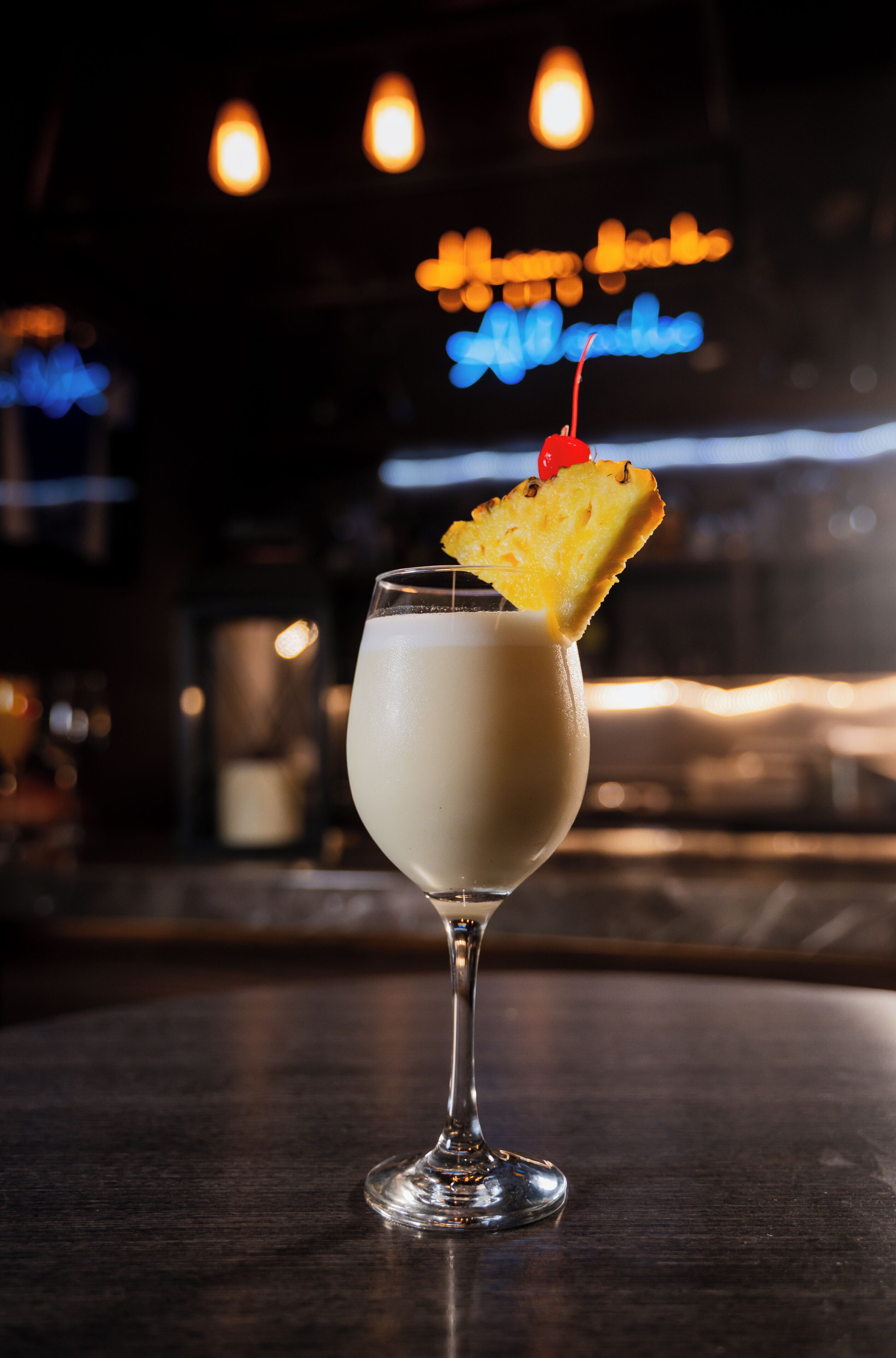A cocktail in a stemmed glass with a pineapple garnish on a bar counter.