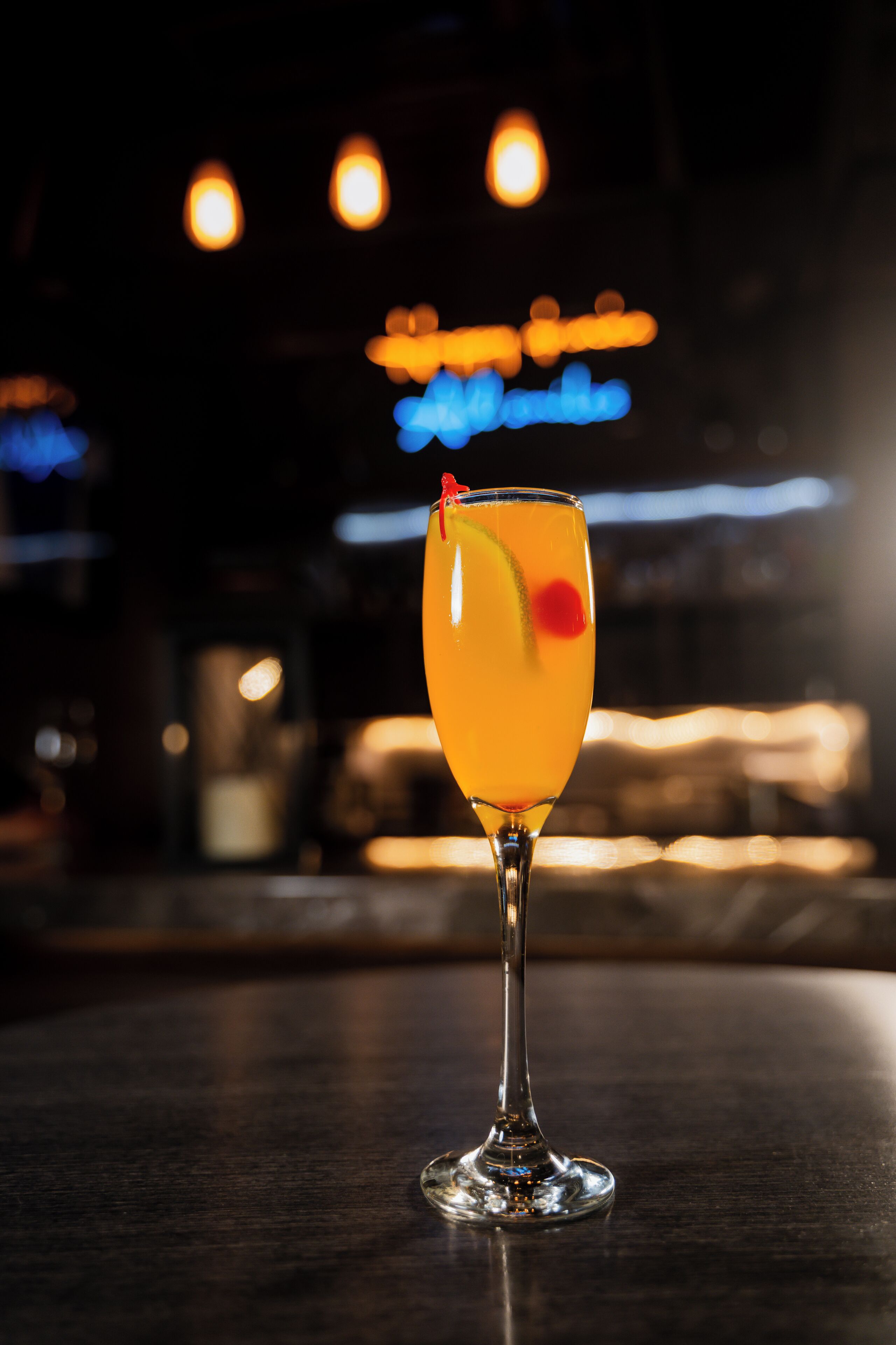 Un verre à cocktail posé sur le comptoir d’un bar, avec des lumières floues en arrière-plan.