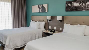 Habitación de hotel con dos camas, una mesita de noche con teléfono, decoración en la pared y una ventana con cortinas.