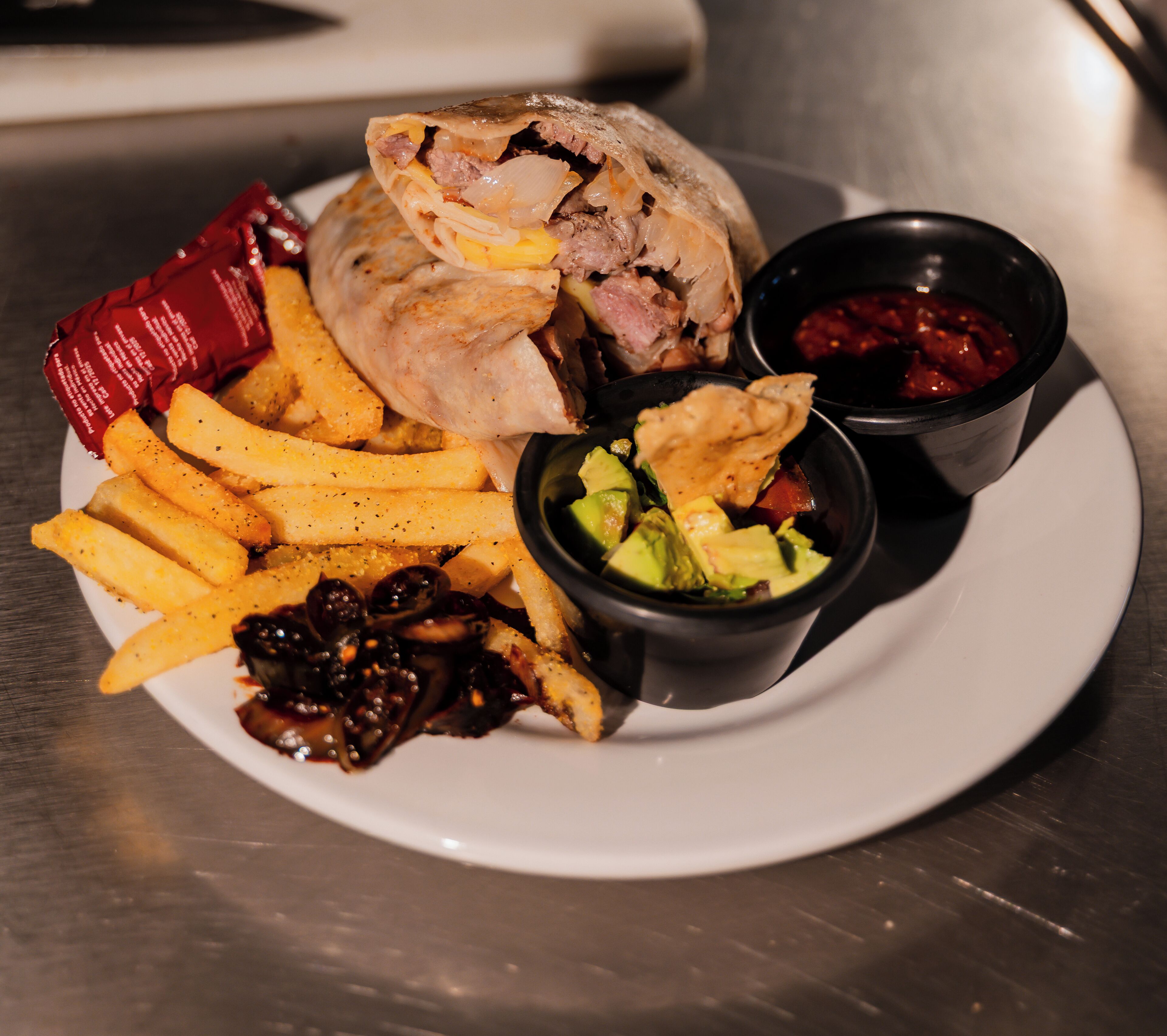 Un plato con un wrap, papas fritas y dos recipientes pequeños de salsa.