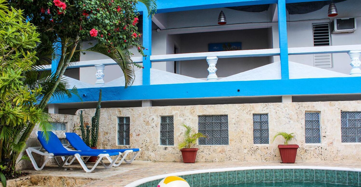 A pool area with blue lounge chairs, a pool with a tiled edge, and a building with a blue and white facade.