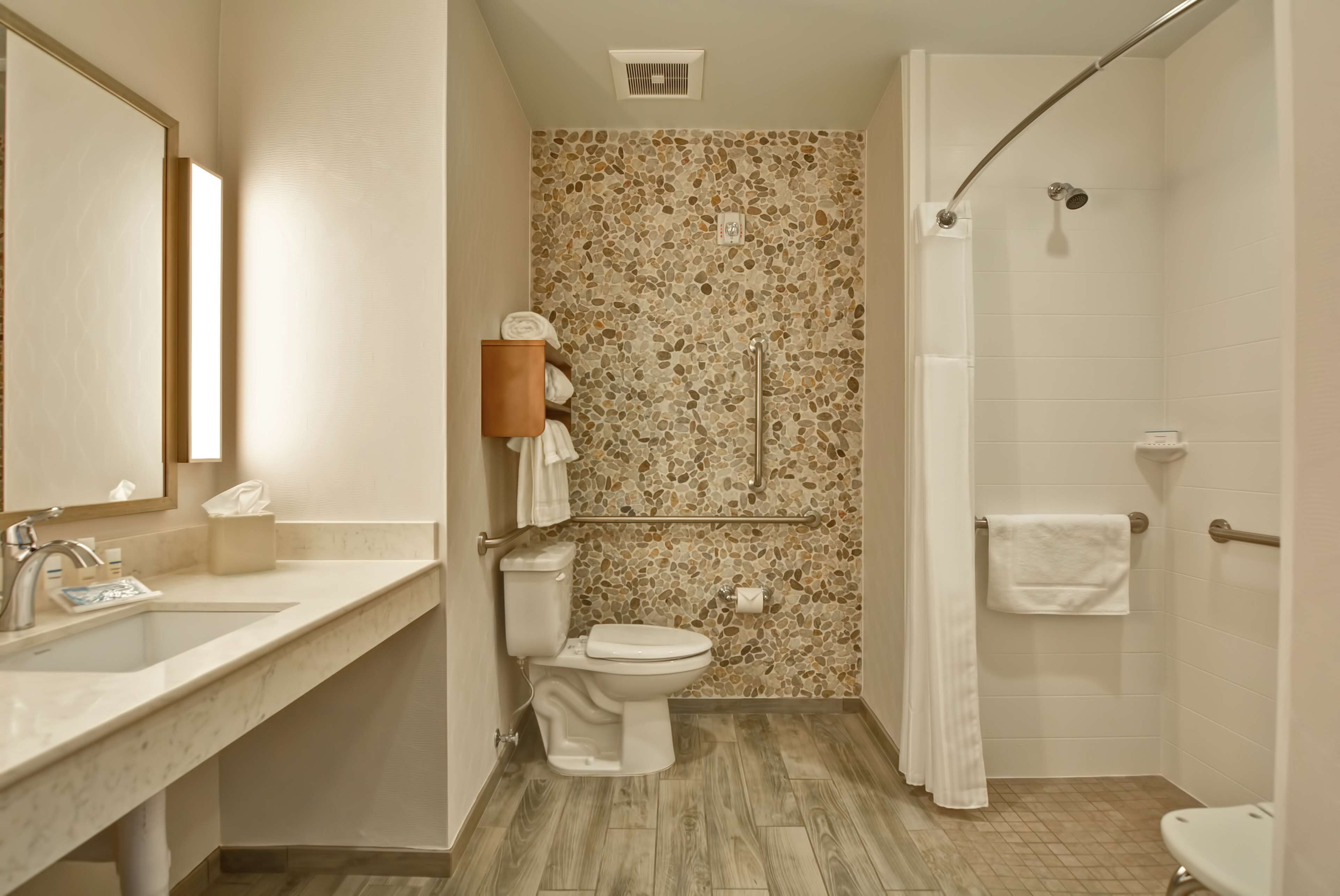 Un baño con lavamanos de mármol, inodoro, ducha con puerta de cristal y pared de mosaico.