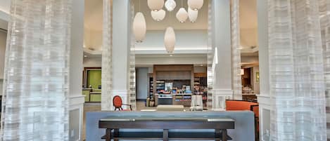 En rymlig lobby med en receptionsdisk, en sittgrupp och utsikt över skylten för Hilton Garden Inn.
