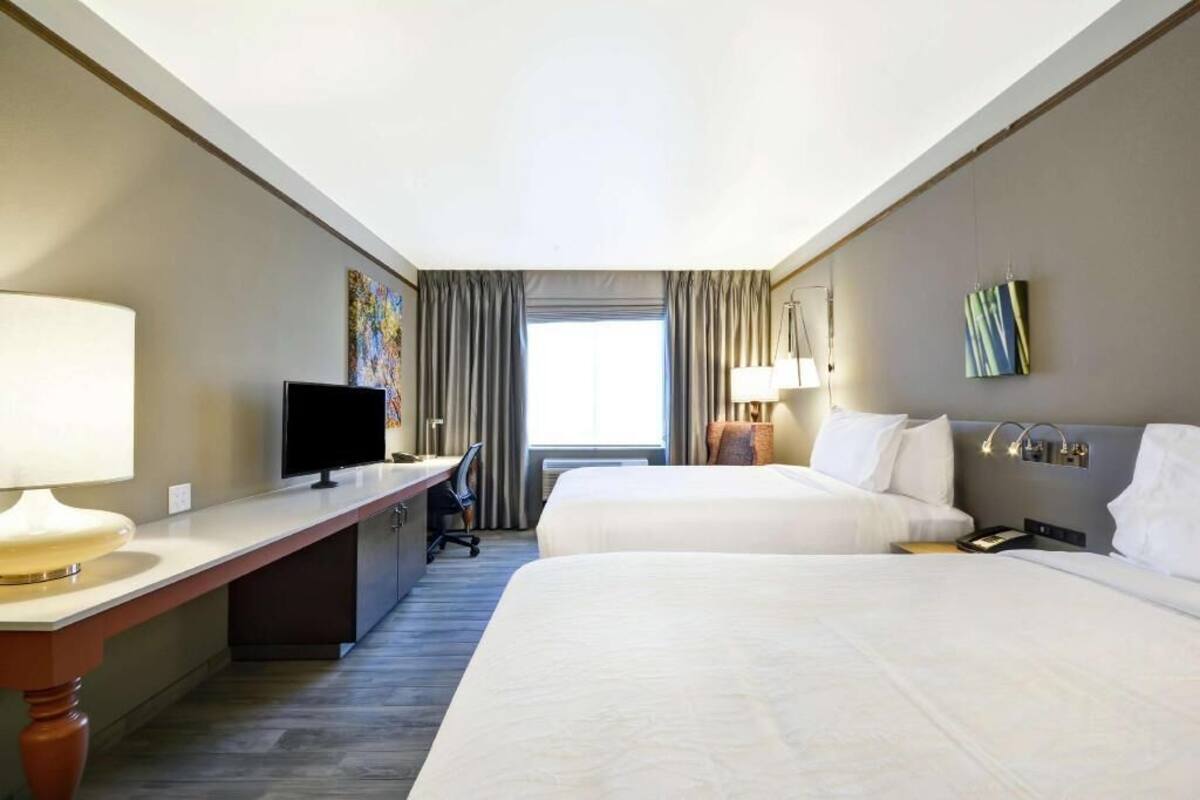 A hotel room with two beds, a desk with a TV, a lamp, and a painting on the wall.