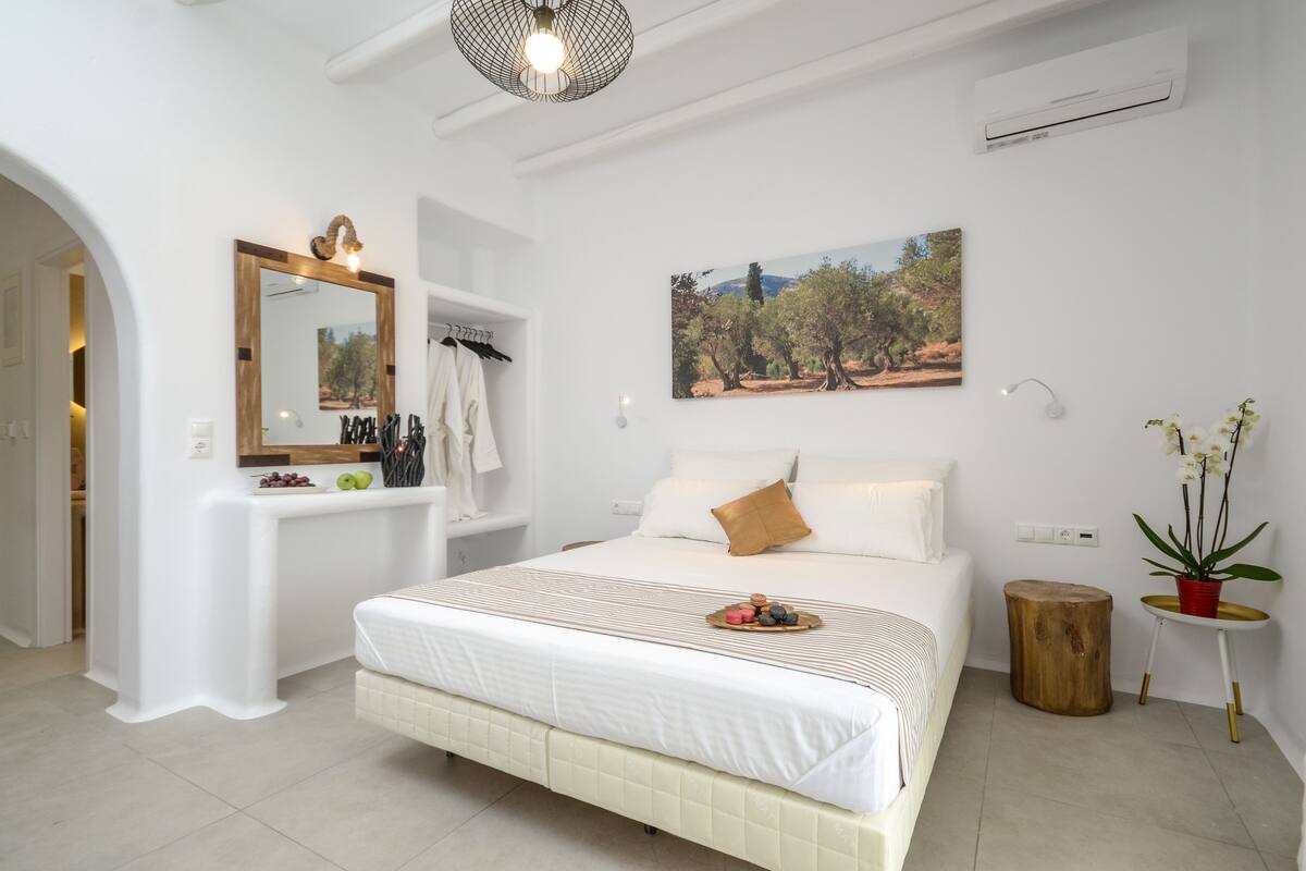 A bedroom with a large bed, a vanity with a mirror, a painting, and a potted plant.