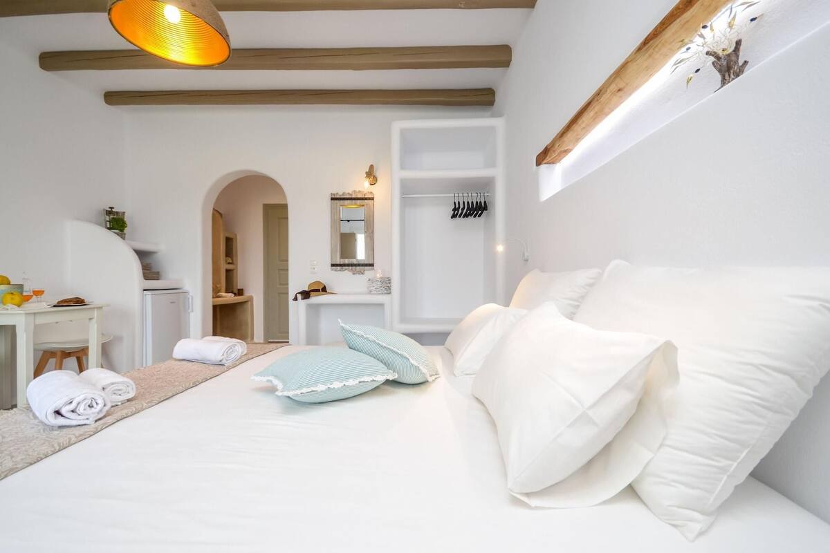 A bedroom with a bed, a desk, a chair, a mirror, and a hanging light fixture.
