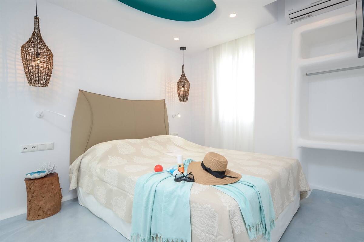 A modern bedroom with a large bed, two hanging wicker lamps, a small wooden stool, and a wall-mounted air conditioner.