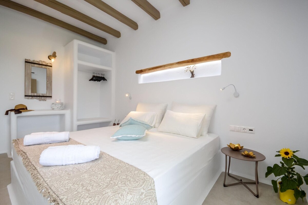 A bedroom with a bed, bedside table, mirror, and a small table with a plant.