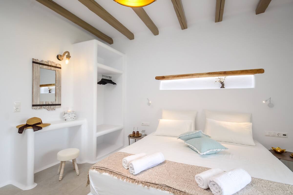 A bedroom with a bed, bedside tables, a vanity, a mirror, and a hanging light fixture.