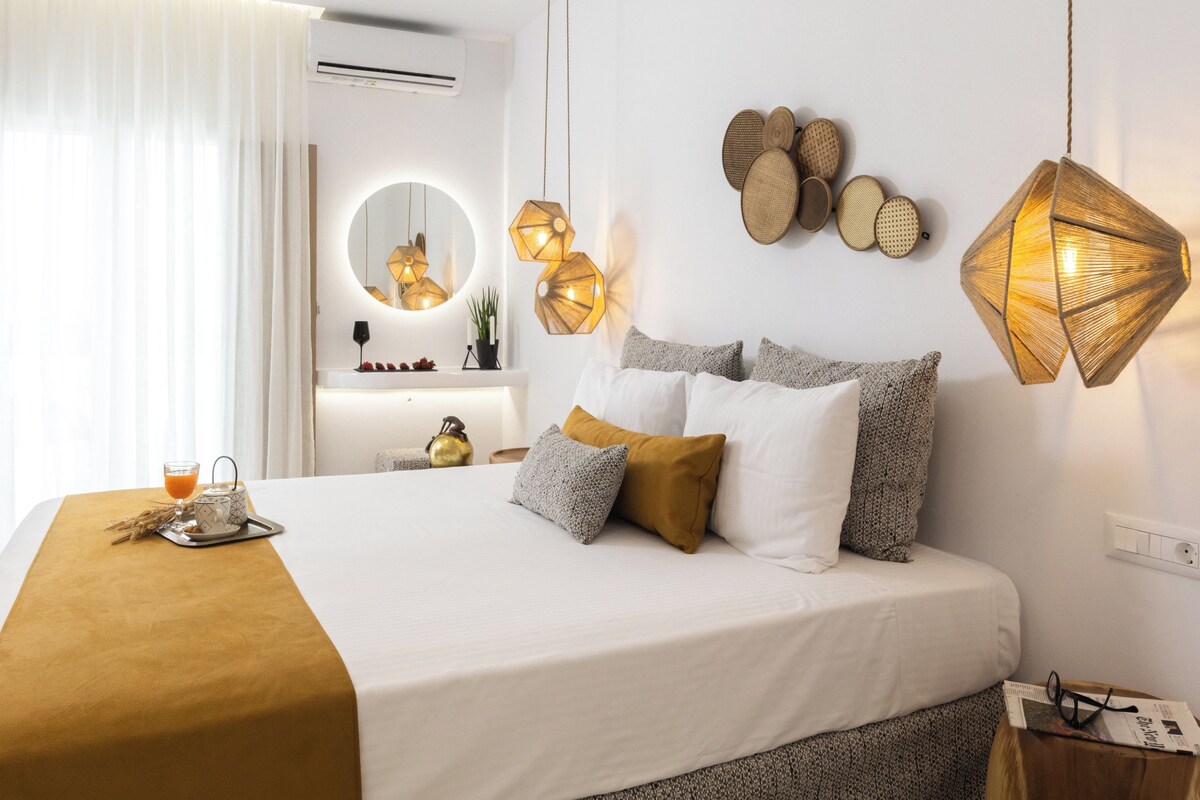 A modern hotel room with a large bed, a bedside table, a mirror, and a hanging light fixture.