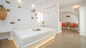 A modern bedroom with a white bed, a breakfast tray, a dining area with orange chairs, and a unique wall design. - Ktima Lino (Naxos)